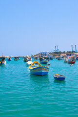 Obraz premium Malta Republic, Malta Island. 25.05.2023. Marsaxlokk city, The harbour and beautiful bright coloured boats on a hot sunny day.
