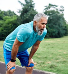 Portrait of a mature mid age man exercising in a park, tired mature female running and taking a...