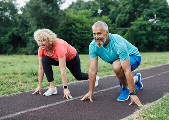 Smiling active mid aged couple standing in start position,  jogging running and walking doing...
