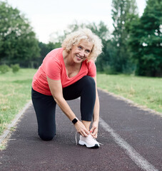 Portrait of a mid age mature sport woman smiling happy and confident, prepering for exercise, tying...