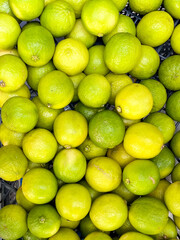 Fresh green limes piled together in a vibrant display, showcasing their smooth texture and bright color, highlighting the abundance of citrus fruits in a market setting