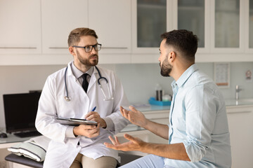 Serious young doctor listening to patient complaints with empathy, engagement writing notes, making...