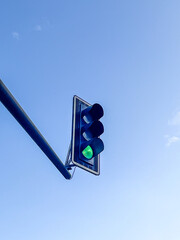 Green traffic light signaling safe passage for vehicles against a clear blue sky, showcasing urban...