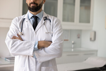 Serious Latin healthcare professional man in lab coat and stethoscope standing in clinic office...