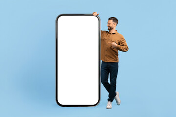Smiling young man pointing at huge blank screen of giant smartphone mockup. Studio shot concept for app promotion, interface design, or tech services, collage