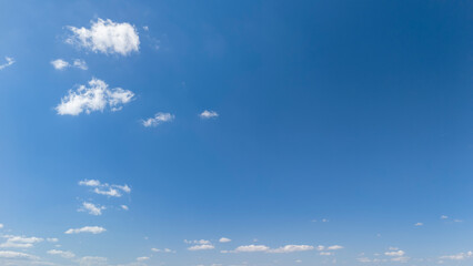 Vast blue sky with scattered fluffy clouds, creating a serene atmosphere. Ideal for backgrounds,...