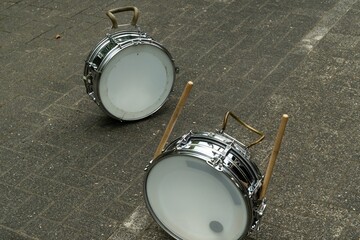 Two marching band snare drums lying on the ground with drumsticks