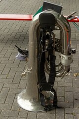 Shiny tuba standing on cobblestone street with harness and cap nearby