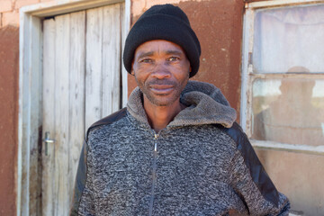 africa village, african man standing outdoors in the yard near the house, wearing a beanie