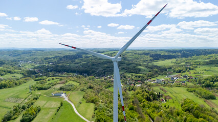 Aerial view of a large wind turbine with rotating blades set against a backdrop of rolling green...