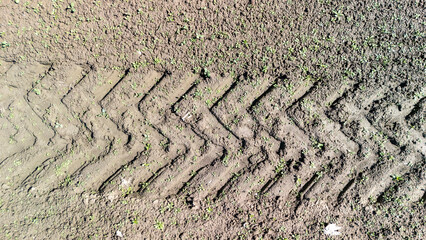 Tire treads create a distinct pattern on freshly tilled soil, reflecting agricultural activity. The...
