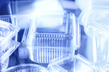 Clear disposable food containers made of plastic, photographed in close-up style, on a reflective surface, representing packaging and sustainability