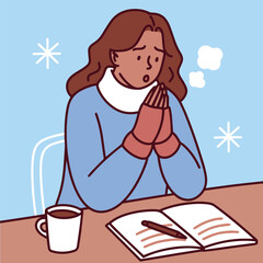 Dark-skinned woman tries to study or work in cold room wearing sweater and holding warm mug near book while snow falls outside