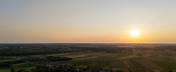 Aerial view of a serene landscape at sunset, showcasing vibrant fields and distant towns, capturing...
