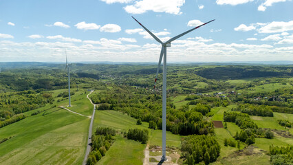 Aerial view of a modern wind farm in a lush green landscape under a bright blue sky. Wind turbines...