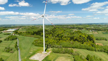 Aerial view of a large wind turbine in a green landscape under a bright blue sky. This renewable...