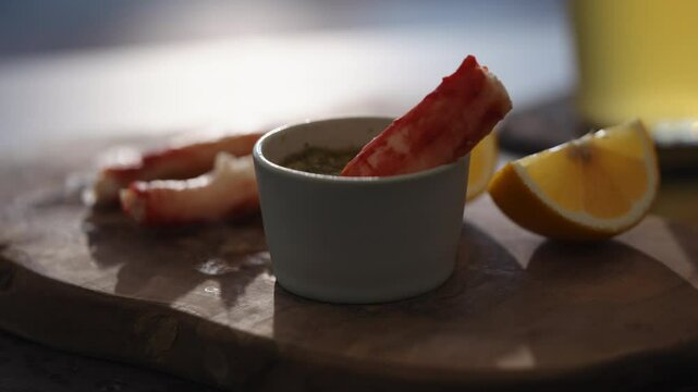 Slow motion gimbal shot of crab leg meat on a olive board with sweet lemon and dip sauce on concrete countertop