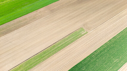 Aerial view of textured agricultural fields showcasing vibrant green and brown patches at daylight,...