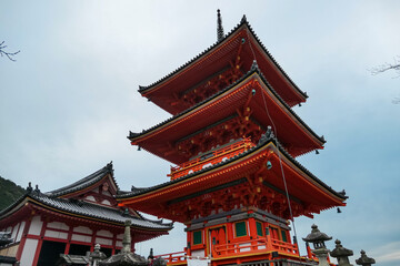 Naklejka premium A dramatic low-angle shot emphasizes the grand scale of the iconic, multi-tiered red pagoda at Kiyomizu-dera Temple, its impressive wooden structure towering against a pale sky in Kyoto, Japan.