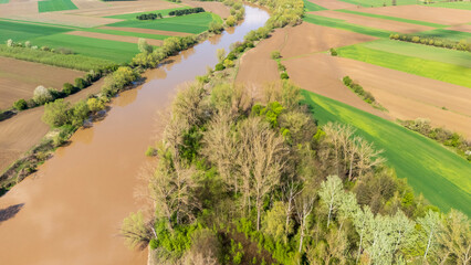 Aerial view of a winding river bordered by lush greenery and patchwork farmland under bright...