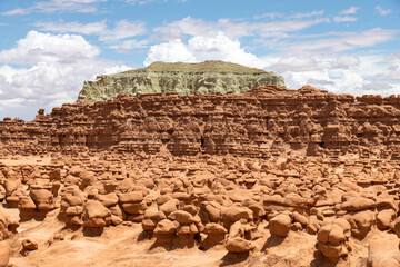 Mushroomlike sandstone rock formations called goblins and eroded cliffs in Goblin Valley State Park, Utah, USA against a white clouded blue sky