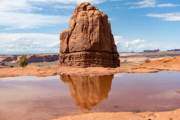 Sandstone formations seen from La Sal Mountains Viewpoint in Arches National Park, Utah, USA with rock formation reflected in pool of water and with balanced rock in far distance