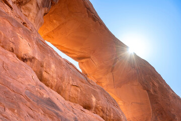 Low angle view of landmark geological sandstone formation Skyline Arch against a blue sky with a bright sun with sun rays just shining above the rim on top in Arches National Park, Moab, UT, USA