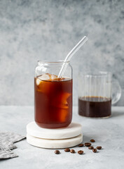 Cold brew coffee in a glass with ice on a marble stand on a light concrete background