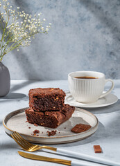 Chocolate brownie with nuts on a plate on a light background with cup of coffee, bouquet of flowers