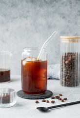 Cold brew coffee in a glass with ice on a light concrete background with coffee beans and spoon.