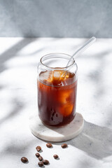 Cold brew coffee in a glass with ice on a light concrete background with coffee beans