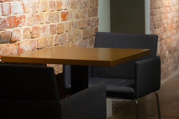 A quiet, stylish lounge area in a cafe with a mustard-colored table, dark upholstered chairs, and exposed brick walls in soft lighting.
