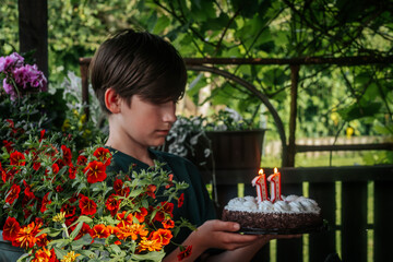 A boy holds a decorated strawberry cheesecake cake with chocolate on the edge. The 11th candle is...