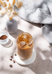Ice latte coffee in a glass with milk on a light background with coffee beans, dry bouquet flowers