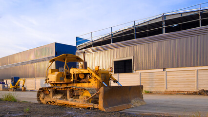 The old bulldozer tractor on the ground in front of industrial warehouse factory building structure in construction site, perspective side view