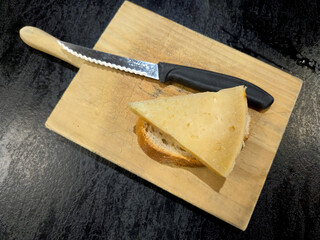 Triangle cheese slice on bread with knife on wooden board. World Cheese Day. Spanish tapas