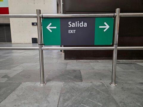 Exit sign with arrows to the right and left and translation into English and Spanish at the station. Emergency exit sign with bilingual directions in modern commercial space