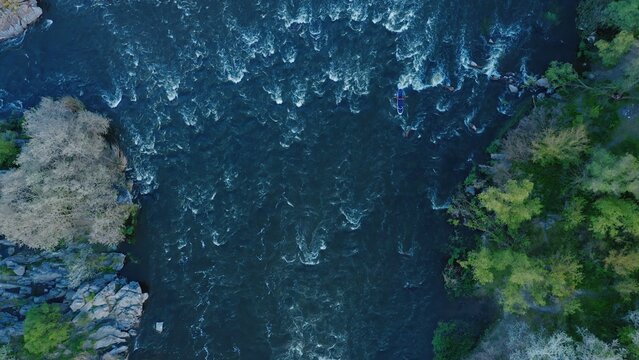 A top-down aerial view of a kayak floating on a turbulent river between forest and stone cliffs.
