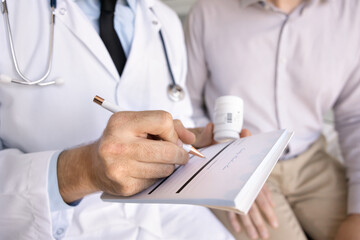 Male physician doctor prescribing pills to patient, writing in paper prescription, holding bottle...