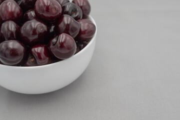 Fresh dark cherries in ceramic bowl on neutral gray cloth – minimal food photography
