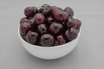 Fresh dark cherries in ceramic bowl on neutral gray cloth – minimal food photography