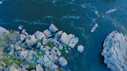 Top down view of two kayaks navigating through a narrow rocky river pass surrounded by large...