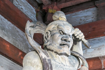 A powerful ancient Nio guardian statue, a fierce wooden protector known as Ungyō, stands guard at a temple gate in Kyoto, Japan, its detailed carving showcasing traditional Japanese Buddhist artistry.
