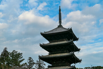Upper tiers of the ancient five-story wooden pagoda at Ninna-ji Temple showcase intricate architectural details against vast, cloudy blue sky, highlighting the grandeur of this famous Kyoto landmark.