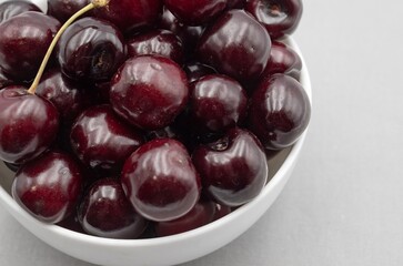 Fresh dark cherries in ceramic bowl on neutral gray cloth – minimal food photography