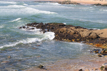 Rocky coastline with sea waves splashing on the shore under bright daylight. Natural marine...