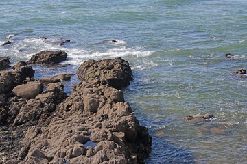 Rocky coastline with sea waves splashing on the shore under bright daylight. Natural marine...