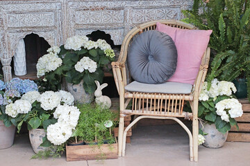 Cozy outdoor decor with a bamboo chair, soft cushions, and white hydrangeas creating a relaxing...