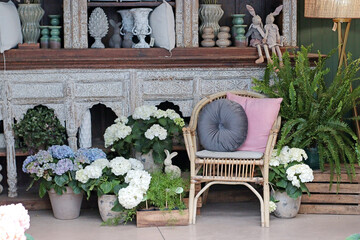 Cozy outdoor decor with a bamboo chair, soft cushions, and white hydrangeas creating a relaxing...