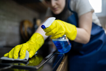 Cleaning kitchen surface with spray cleaner and cloth during daytime